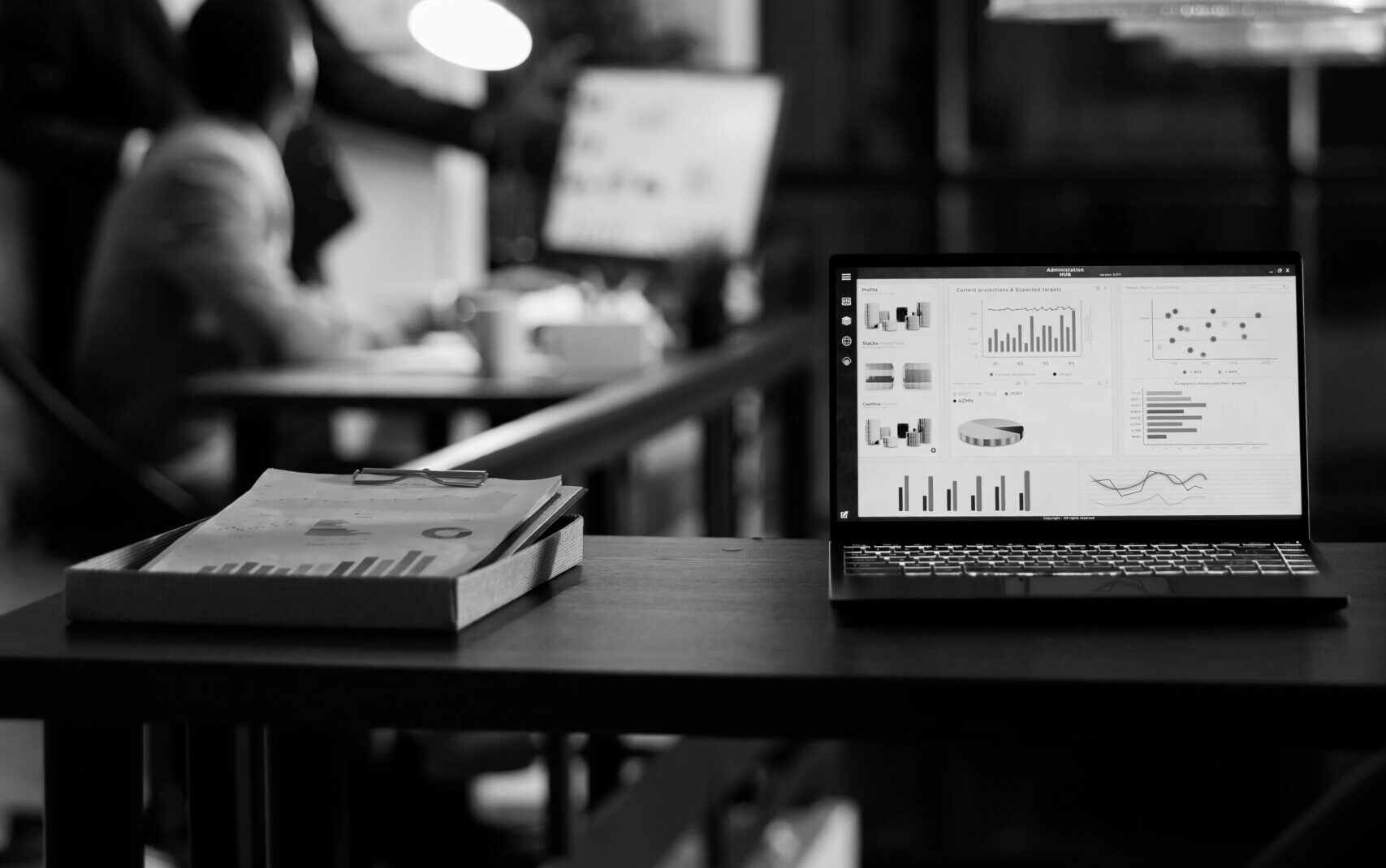 laptop-computer-with-financial-graphs-screen-standing-table-startup-office-coworkers-discussing-company-strategy-background-employees-working-late-night-startup-office